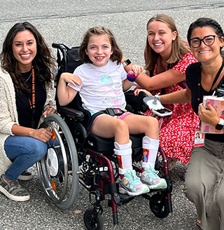 Three women next to a happy girl in a wheelchair