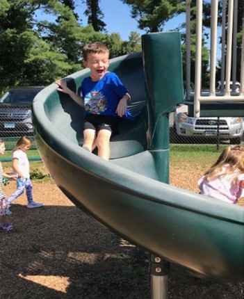Student smiling as he goes down the slide
